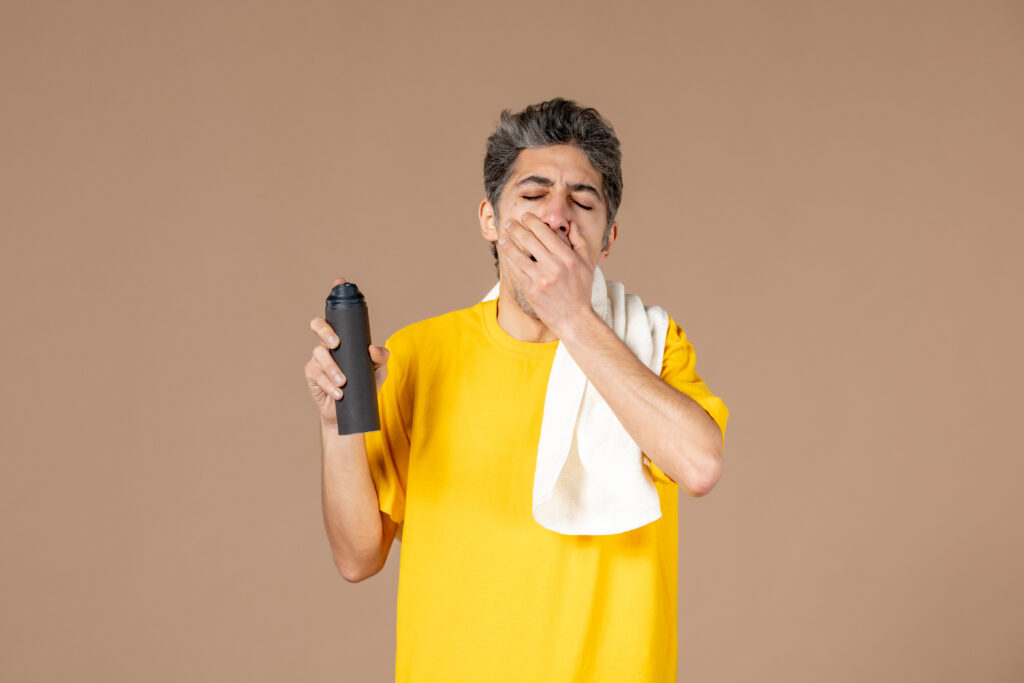 Alt-tekst: "Man knijpt met een hand zijn neus dicht terwijl hij met de andere hand een luchtverfrisser vasthoudt, klaar om een nare geur te bestrijden. Geschikt beeld voor een blog over onaangename geuren en vlekken.